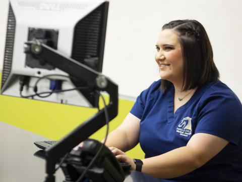 female student in scrubs at a computer